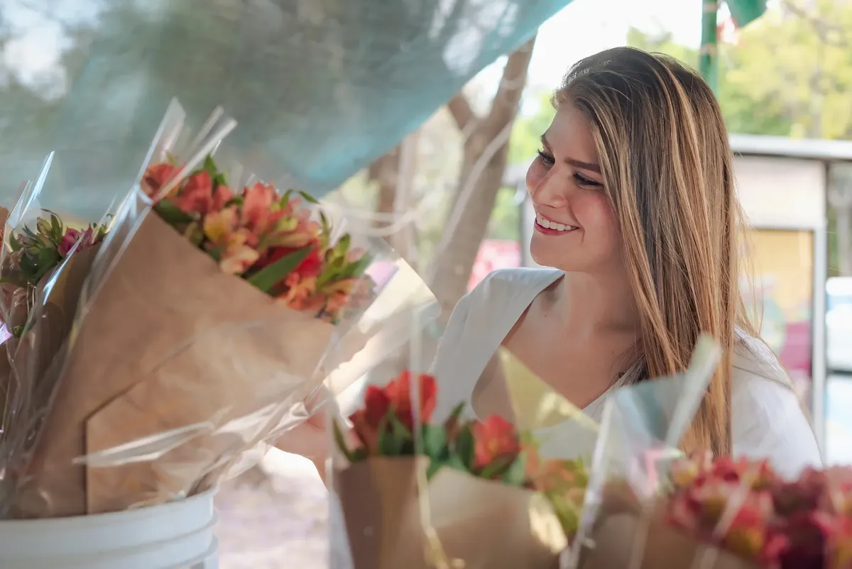 Joyful woman selecting colorful flower bouquets at outdoor market, showcasing natural beauty.